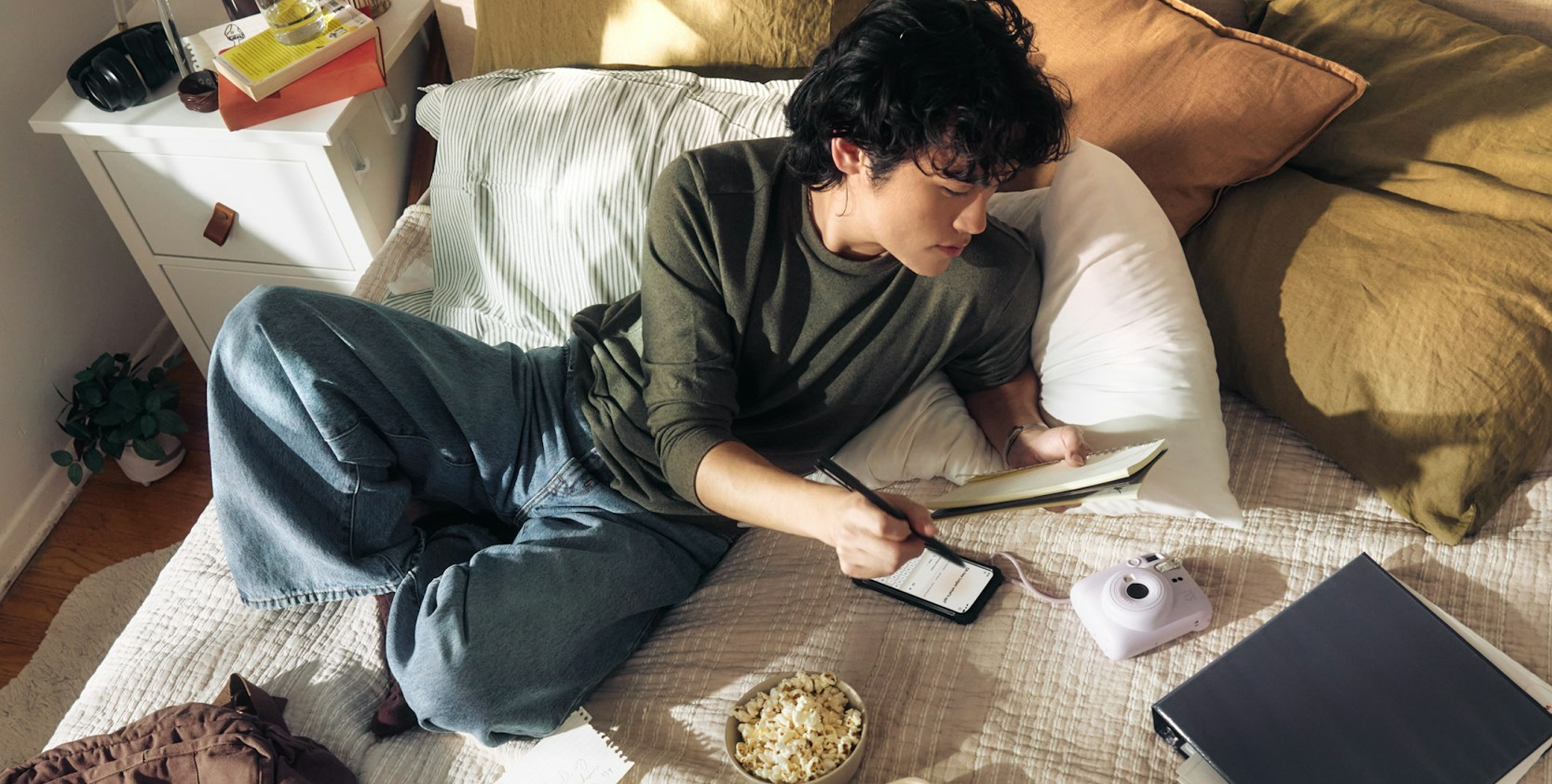 Person laying on their bed using a notepad and a phone